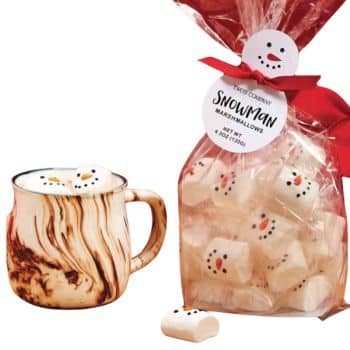 A marble-patterned mug filled with hot chocolate topped with snowman-shaped marshmallows. Next to it is a clear bag containing more marshmallows, decorated with a snowman face and tied with a red ribbon.