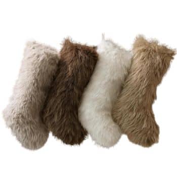 Four fuzzy Christmas stockings in shades of gray, brown, off-white, and tan are lined up in a row. They are made from a soft, fur-like material, giving a cozy and festive appearance.