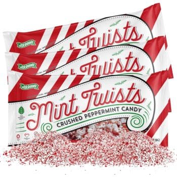 Three packages of Mint Twists crushed peppermint candy are arranged with the contents spilling out in front. Perfect for Christmas treat recipes, the packaging features red and white stripes with green accents.