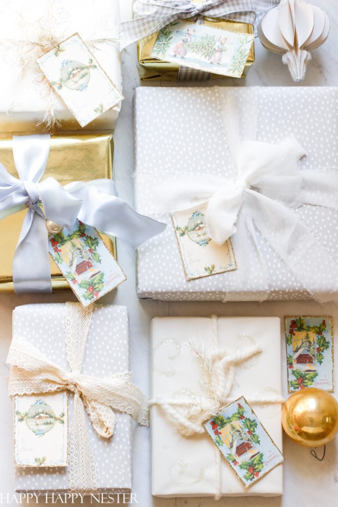 A collection of beautifully wrapped holiday gifts with cute Christmas tags and various ribbons. Packages feature white, gold, and patterned paper, topped with lace and bows. A gold ornament adds a festive touch to the arrangement.