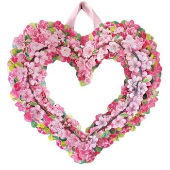 A heart-shaped floral wreath made of pink blossoms and green leaves, with a hollow center. It is hung with a pink ribbon.