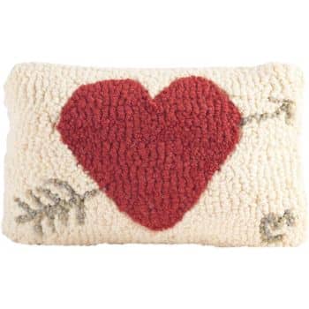 A rectangular, textured pillow with a large red heart design in the center. An arrow is drawn through the heart, and the background is a soft, off-white color.