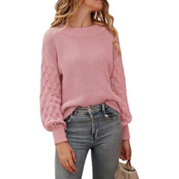 Woman wearing a knitted pink sweater with textured sleeves and light blue jeans, holding a beige bag.