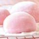 Close-up of Easy Mochi, pink desserts dusted with powdered sugar, resting on a metal cooling rack. The soft, round mochi have a smooth texture and gentle light pink color, evoking a sweet and delicate treat.