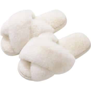 A pair of fluffy, white slippers with crisscross straps across the top. Their plush texture suggests comfort and warmth. The soles appear soft, making them suitable for indoor use.