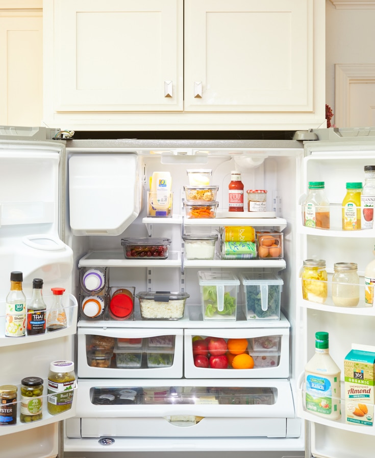 Open refrigerator filled with various foods and beverages. Shelves, arranged using professional organizing tips, hold containers, eggs, and vegetables, while the door racks neatly store sauces, drinks, and condiments. The fridge appears organized and well-stocked.