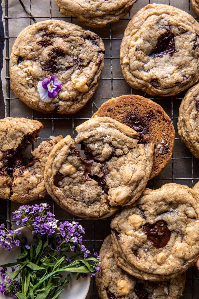 A delightful scene of chocolate chip cookies with melted chocolate chunks on a cooling rack. One cookie is adorned with a small purple flower, while a bouquet of purple flowers adds charm beside it, offering inspiration for recipes made with chocolate chips.