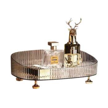 A glass tray holds three perfume bottles, one is rectangular, one is cylindrical, and the third has a decorative deer head lid. The tray has ribbed sides and stands on small golden feet.