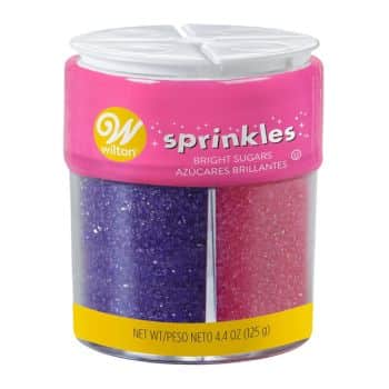 A clear container of Wilton bright sugar sprinkles with a pink lid is perfect for enhancing your pink desserts. It features two sections, one with purple sugar and the other with pink sugar. The label displays the product name and weight, adding both flair and flavor to your treats.