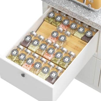 A neatly organized kitchen drawer filled with small uniform jars of spices, each topped with a metal lid and round label. Using professional organizing tips, the jars are arranged in rows on a light wooden insert, showcasing a vibrant spectrum of colorful spices.