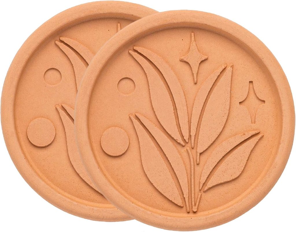 Two circular terracotta disks with a carved design of leaves and geometric shapes could easily inspire recipes made with chocolate chips. Their minimalist style, featuring two leaves and decorative dots and stars, evokes an organic elegance reminiscent of artisanal baking creations.