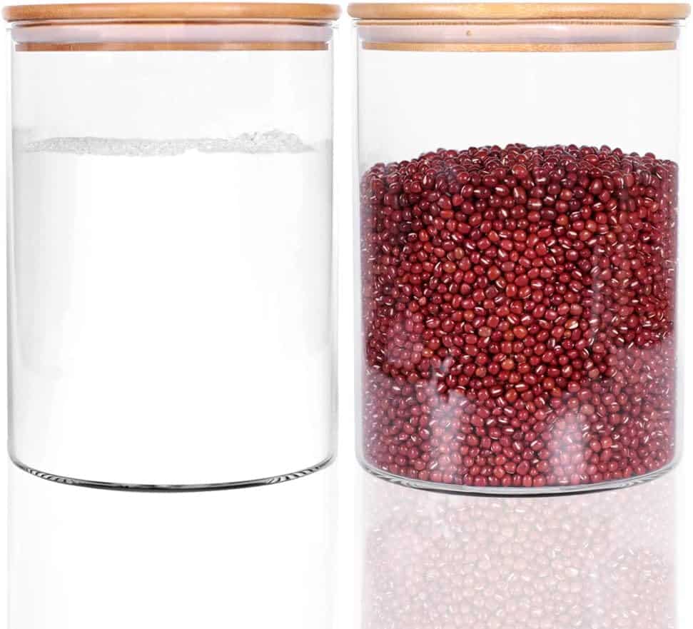 Two transparent glass jars with wooden lids are displayed. The left jar is empty, while the right brims with red beans. Both sit on a reflective surface, exemplifying professional organizing tips for a tidy and visually appealing kitchen space.