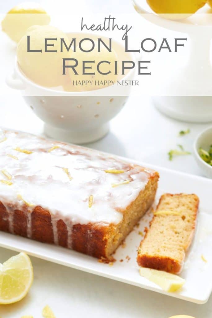 A moist lemon loaf with white icing rests on a rectangular plate, surrounded by scattered lemon slices and more lemons in the background. Text over the image reads "Healthy Lemon Loaf Recipe - Happy Happy Nester." This delightful treat is perfect for a health-conscious sweet craving.