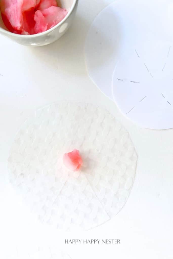 A thin round sheet of rice paper with a small amount of pink filling on it. Another rice paper sheet is drawn with cutting guides, and a bowl containing more pink filling is partially visible at the top. Text at the bottom reads, "HAPPY HAPPY NESTER.