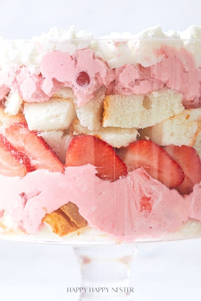 A delightful easy fruit trifle recipe features a dish filled with layers of white cake, pink whipped cream, and sliced strawberries, crowned with a layer of white whipped cream.