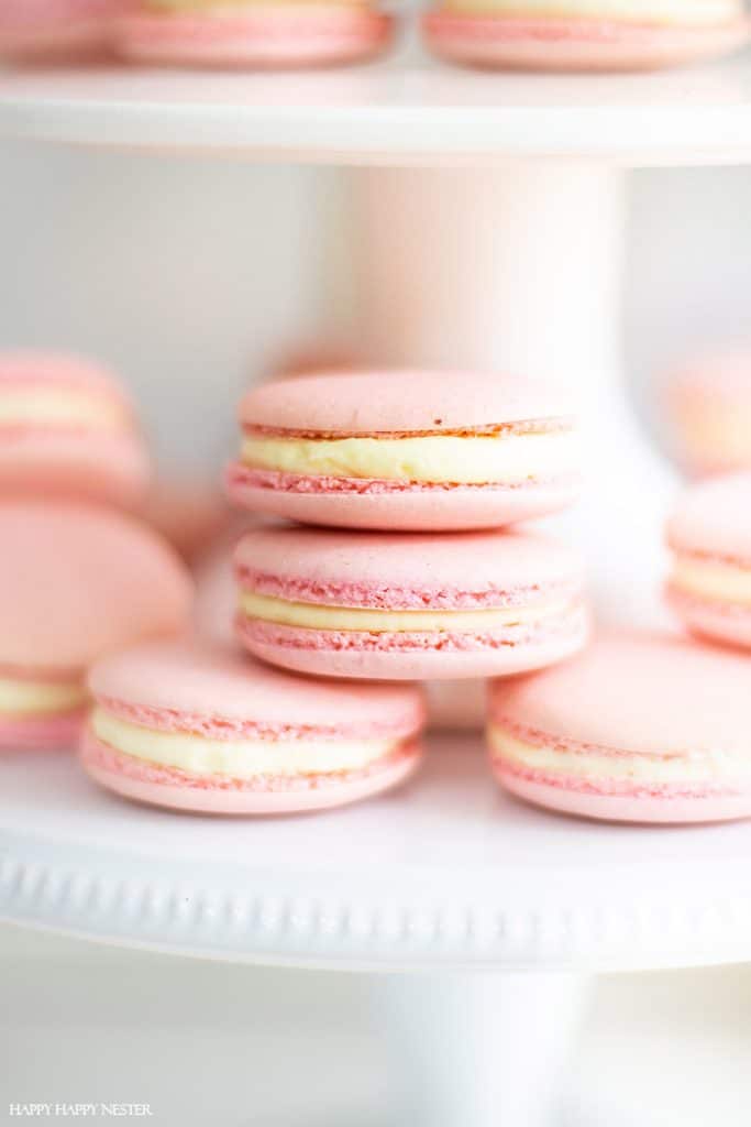 Close-up of exquisite pink desserts, featuring macarons with creamy filling stacked elegantly on a white cake stand, creating a visually appealing display.