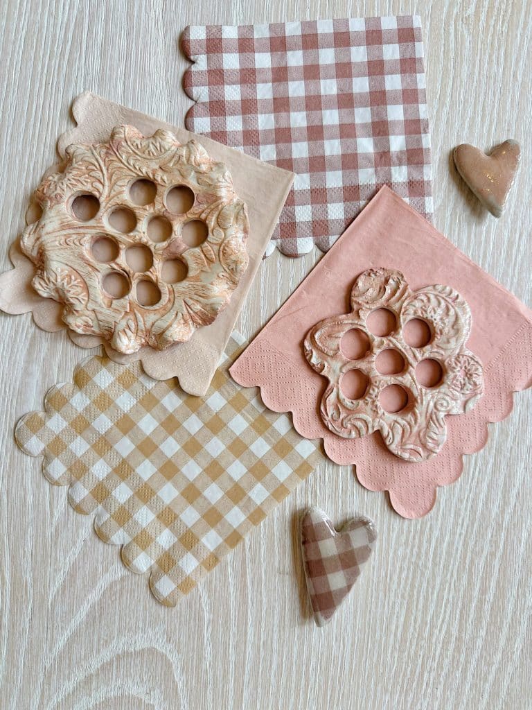 Clay flower-shaped stamps resting on pink and brown plaid napkins, embodying my favorite spring crafts. Nearby, two plaid heart decorations add charm to this cozy, rustic scene set on a light wood surface.