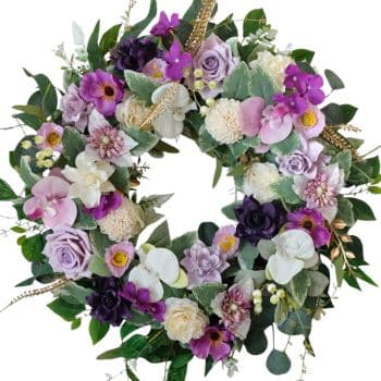 A circular floral wreath composed of various flowers in shades of purple, white, and pink. It includes roses, orchids, and greenery, creating a lush, vibrant arrangement.