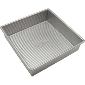 A metal square baking pan with ribbed sides and base, perfect for creating my favorite desserts. The shiny, non-stick interior ensures cakes or brownies come out effortlessly. Its simple, functional design makes it an essential tool for any dessert lover.