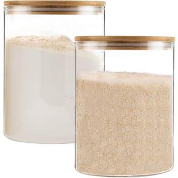 Two glass jars with bamboo lids resemble the ingredients of my favorite desserts. The front jar is filled with a light brown granular substance, while the back jar contains a white powder. Both jars are clear and cylindrical.