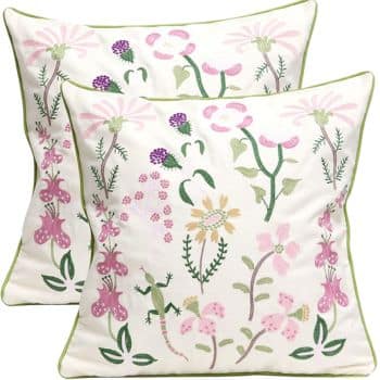 Two white throw pillows featuring colorful embroidered floral designs in shades of pink, purple, and green. Each pillow has green piping around the edges and displays whimsical flowers and plants in a playful pattern.