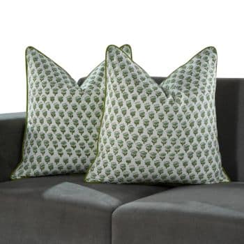 Two decorative pillows with green leaf patterns are placed on a dark gray sofa. The pillows have prominent edges and are positioned at an angle, showcasing their design. The background consists of soft shadows on the sofa.