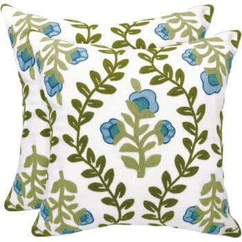 Two decorative pillows feature a white background with a green vine and leaf pattern, interspersed with blue flowers. The design is symmetrical and appears vibrant against the neutral backdrop.