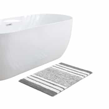 A white bathtub next to a rectangular bath mat with gray and white stripes on a white floor.