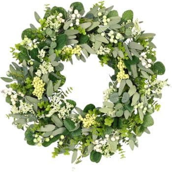 A circular wreath made of various green leaves and small white berries. The foliage includes a mix of eucalyptus and other greenery, giving a lush and natural appearance against a white background.