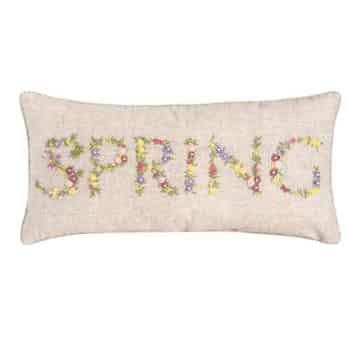 A rectangular cushion with a beige background features the word "SPRING" embroidered in colorful floral patterns.