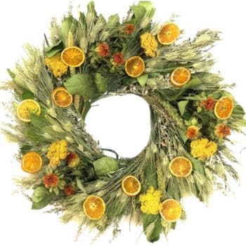 A wreath made of greenery and dried grasses, adorned with slices of dried oranges and clusters of yellow and orange flowers, creating a natural, rustic decoration.