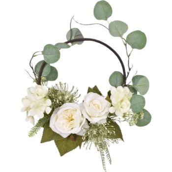 A circular floral wreath featuring white roses, hydrangeas, ferns, and green eucalyptus leaves, all arranged symmetrically on a dark ring.