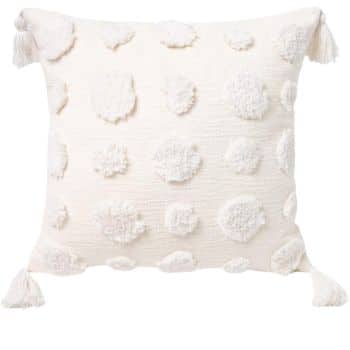 A square decorative pillow with a textured pattern of fluffy, circular tufted designs in off-white. Each corner features a cream-colored tassel, adding a touch of elegance. The background is plain white.