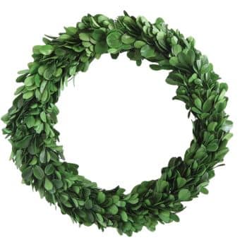 A circular wreath made of lush green leaves. The leaves are tightly woven together, forming a thick, verdant ring. The background is plain white, highlighting the wreath’s vibrant color and natural texture.