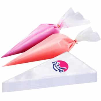 Two filled piping bags, one pink and one red, hover above a stack of transparent piping bags in triangular packaging. A logo with the text "Riccle" is visible on the clear packaging, ready to help you craft my favorite desserts with precision and flair.