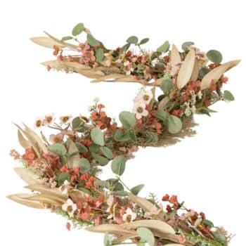 A floral arrangement shaped like the letter "S" featuring a mix of dried leaves, green eucalyptus, and small flowers in shades of red, pink, and cream.