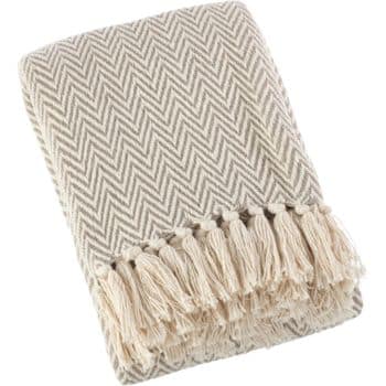 A folded beige and white herringbone patterned blanket with fringe tassels along one edge.