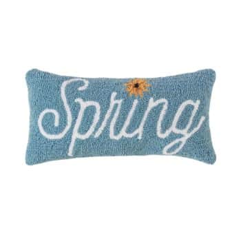 A rectangular blue pillow with the word "Spring" written in white cursive text. There is a small yellow flower with a brown center near the top right corner of the text.