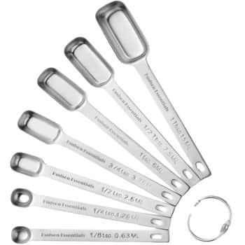 A set of seven stainless steel measuring spoons, perfect for crafting my favorite desserts, is arranged in a fan shape. Each spoon is labeled with measurements from 1 tablespoon to 1/8 teaspoon and includes a metal ring for keeping the spoons together.