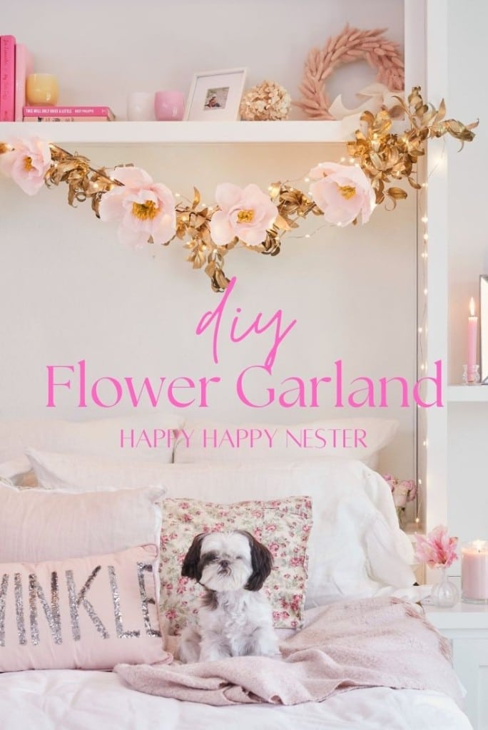 A cozy room with white shelves adorned with pink decor and a DIY flower garland. A small dog sits on a light-colored bed, surrounded by pillows, including one that reads "Twinkle." Text in the image highlights the charm of "Happy Happy Nester.