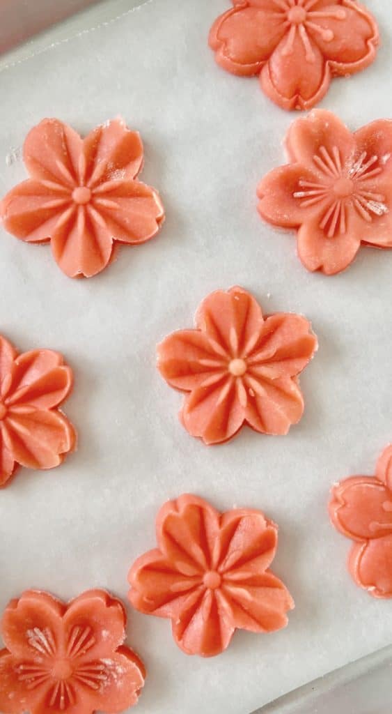 Nine pink flower-shaped cookies, among my favorite desserts, are artfully arranged on a sheet of white parchment paper.