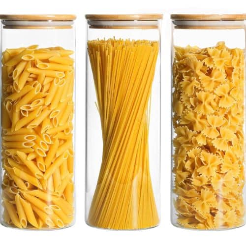 Discover how to organize a small pantry with three transparent glass jars, each crowned with a wooden lid and filled with enticing varieties of uncooked pasta—penne, spaghetti, and farfalle—artfully arranged in a tidy row.