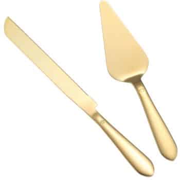 A set of two gold-colored utensils on a white background, perfect for serving the best spring cakes. One is a long, narrow cake knife with a slightly curved blade, and the other is a triangular cake server with a flat, angled surface. Both have smooth, rounded handles.