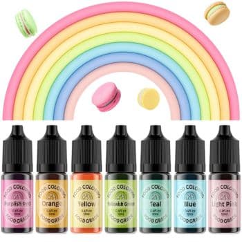 Seven bottles of food coloring (purplish red, orange, yellow, yellowish green, teal, blue, light pink) are lined up below a rainbow arch. Scattered above them are three of our favorite spring cookies—macarons—in delightful shades of pink, green, and yellow.