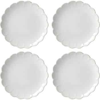 Four identical white porcelain plates with scalloped edges, arranged in a 2x2 grid on a plain background.