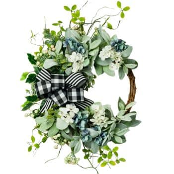 A decorative wreath featuring lush green leaves, small white flowers, and a black-and-white striped ribbon bow. The design includes intertwined vines, creating a fresh and elegant appearance.