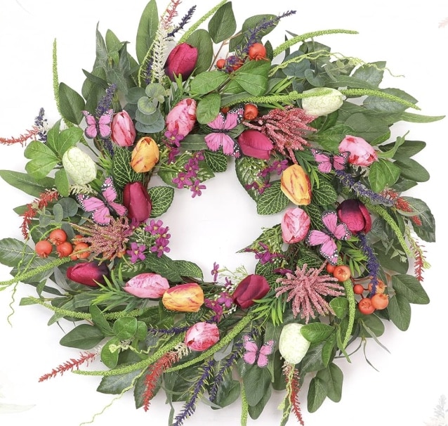 A decorative wreath made of green leaves, colorful tulips in shades of pink, red, orange, and white, purple and red flowers, and small orange berries—perfect as cheerful spring kitchen decor.