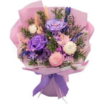 A bouquet with purple roses, white and pink carnations, and greenery, wrapped in pink paper with a purple ribbon.