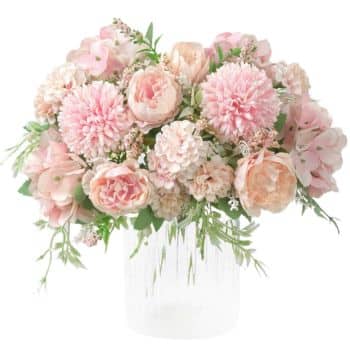 A bouquet of pink and peach flowers, including roses and carnations, arranged in a clear glass vase with green foliage. The flowers are lush and tightly clustered, creating a soft, romantic appearance.