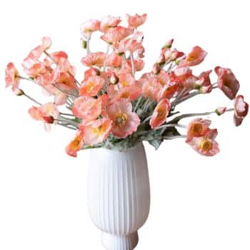 A white vase holds an arrangement of pink and white poppies with green stems. The ceramic vase features vertical grooves, and the flowers have delicate, ruffled petals with yellow centers.